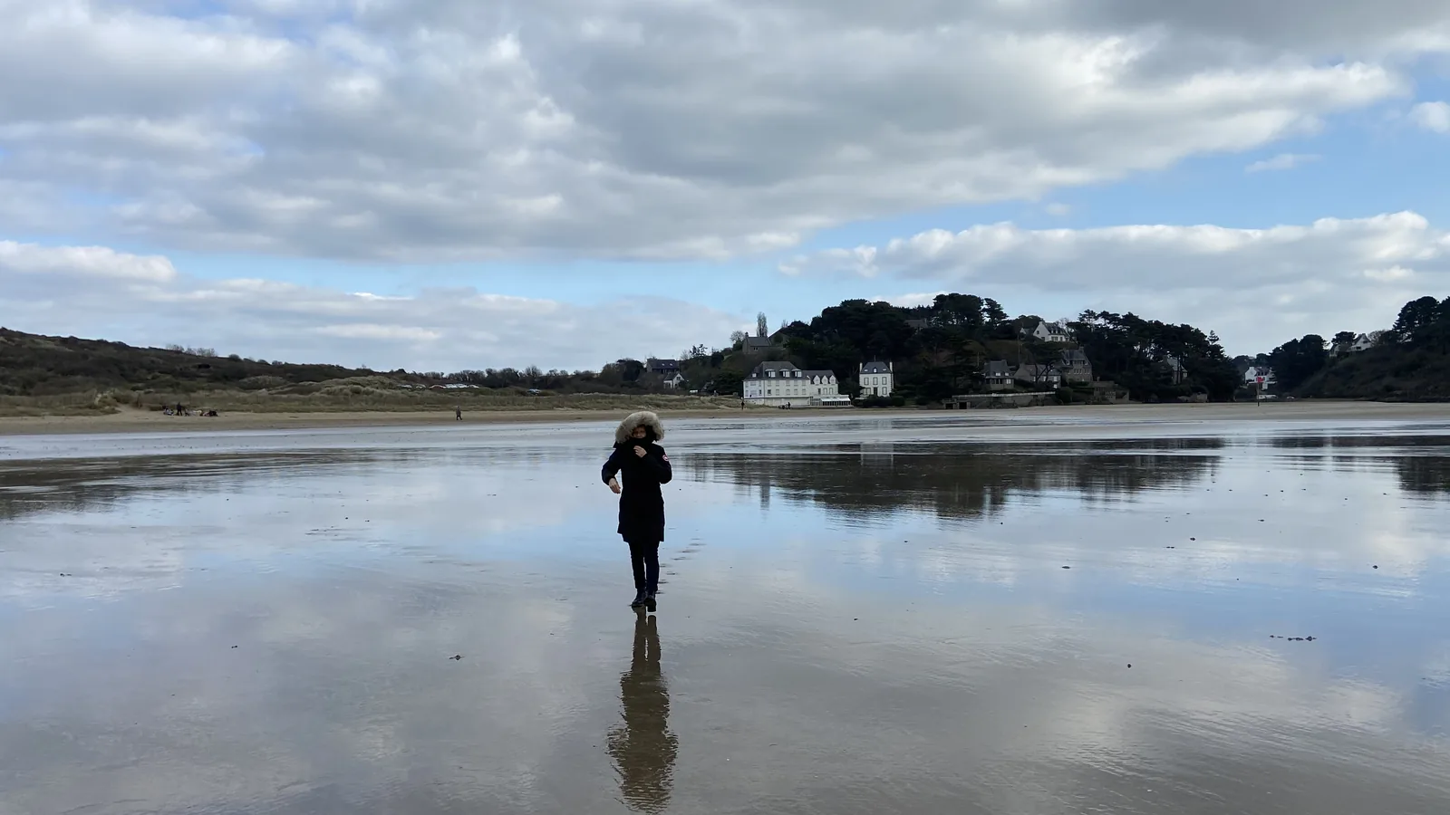 Une silhouette marche sur une plage qui reflète le ciel, en Bretagne
